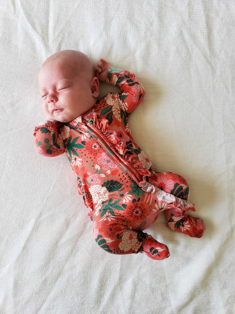 A baby asleep in floral pajamas on a white bed