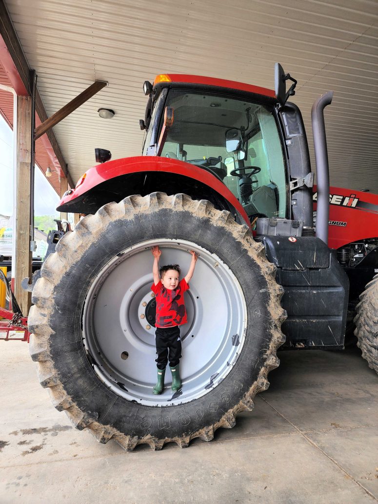 Toddler standing in the wheel well of a tractor