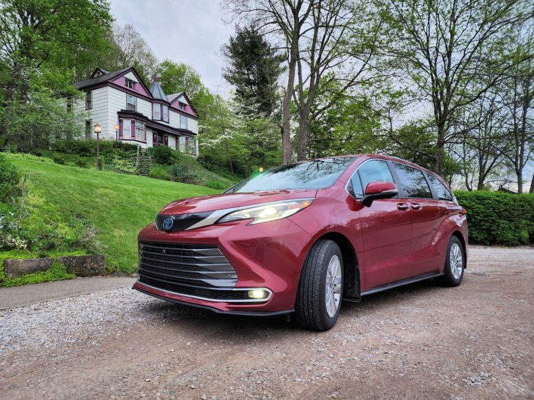 Toyota Sienna in front of a green hill and old house