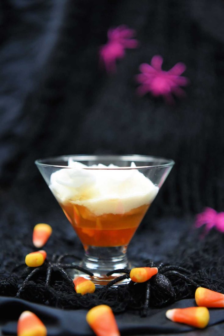 A layered cocktail in a martini glass made to look like a piece of candy corn