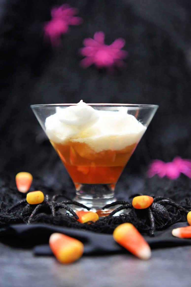 A layered cocktail in a martini glass made to look like a piece of candy corn