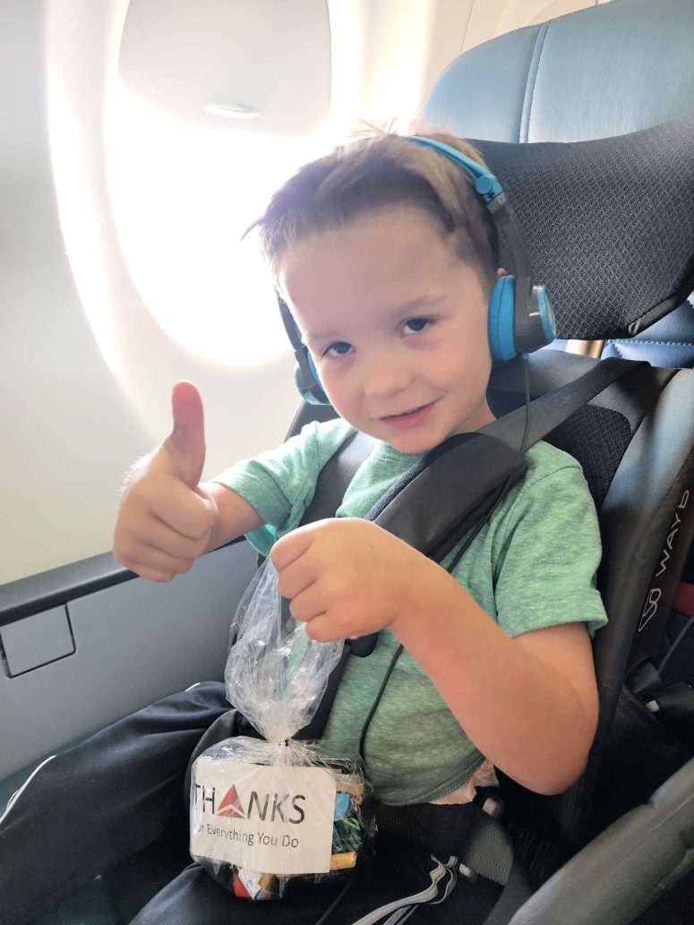 Toddler smiling on an airplane with his thumbs up and holding a gift bag for the flight crew.