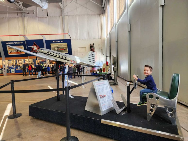 A toddler boy sitting on a demonstration pilot seat at the Delta flight museum