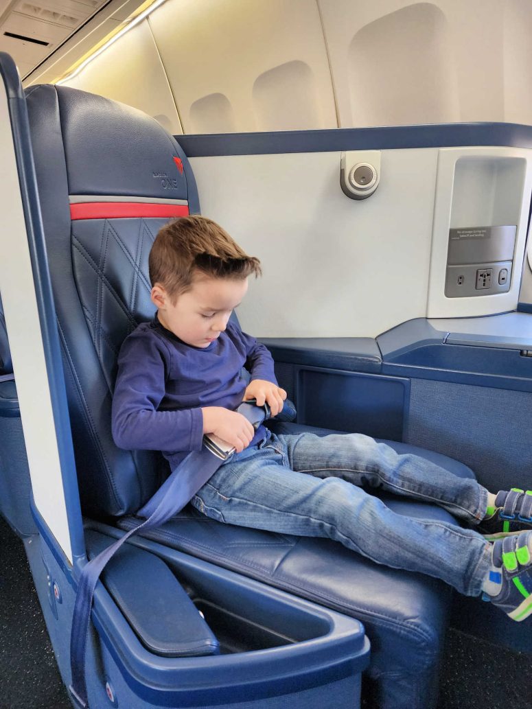 A toddler boy sitting in the Delta One seat at the Delta Flight Museum