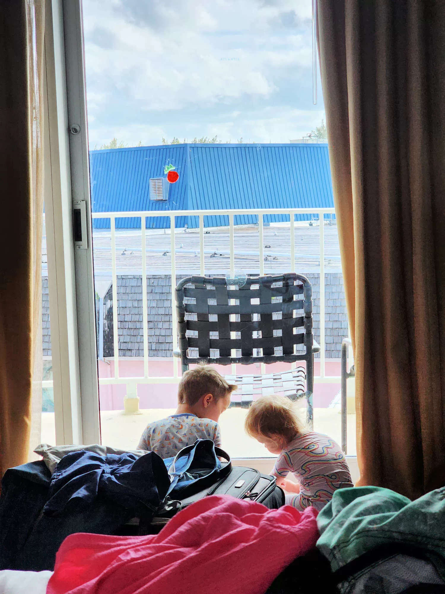 Two young kids play in a hotel room. They are sitting by the window, adding gel clings to the window.